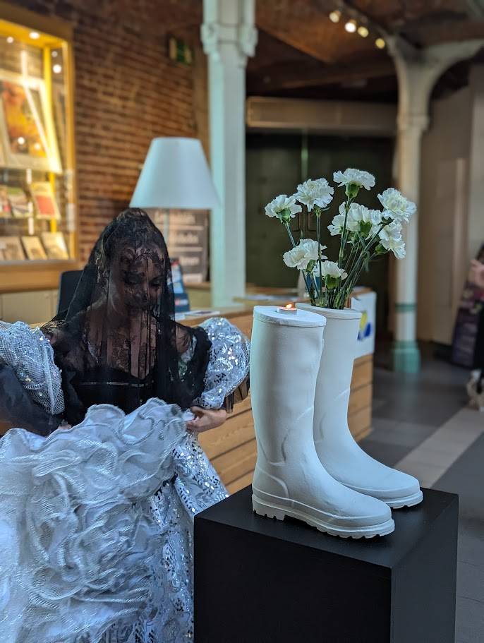 Symbolique des bottes Wilman Gomez Tamayo, Les oubliés — sculpture de deux bottes gauches, Halles Saint-Géry (Bruxelles, 2025).<br />
Cette paire impossible fait référence aux « faux positifs » en Colombie (2002-2008) : des civils exécutés par l’armée, déguisés en guérilleros pour simuler des victoires au combat. Les incohérences — comme des bottes identiques chaussées aux cadavres — ont révélé la mise en scène macabre. Ici, l’artiste transforme ce signe d’artifice en symbole de mémoire et de vérité.</p>
<p>(Photo © Blog de l’art / courtoisie de l’artiste)